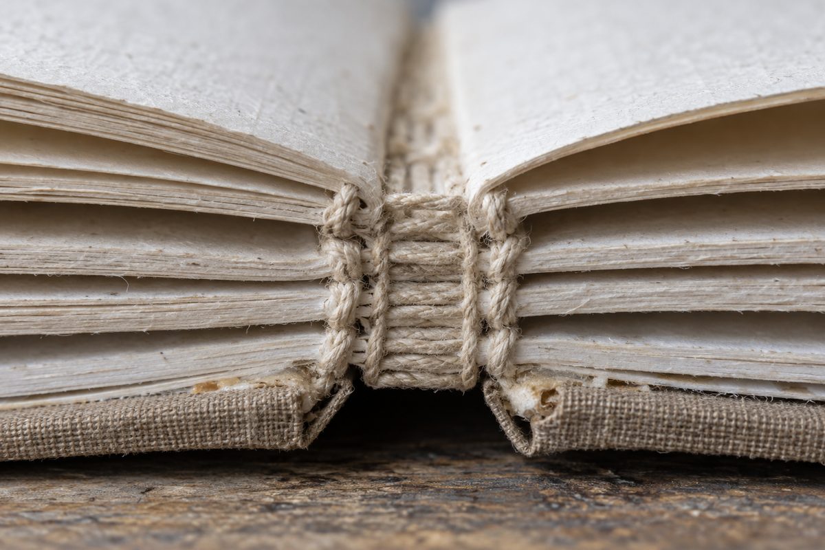 Extreme close-up of hand-stitched linen thread running through folded book signatures