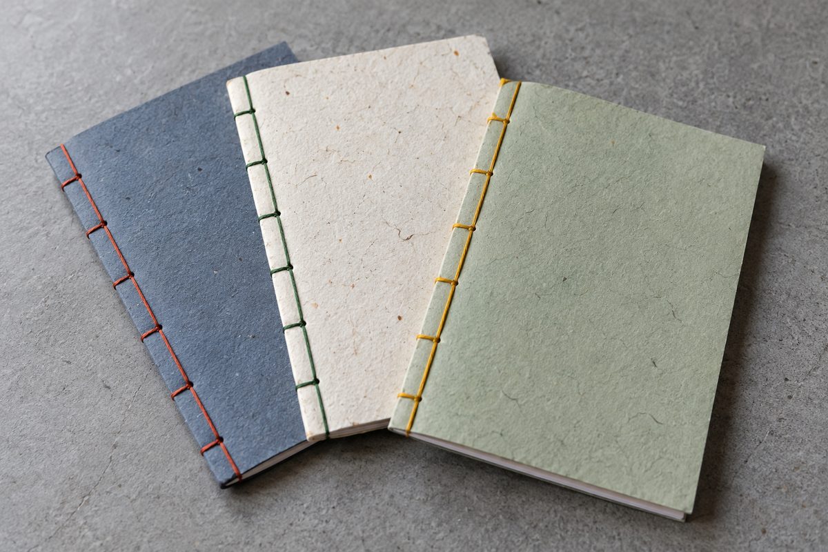 Three slim poetry chapbooks with hand-torn deckled edges and exposed stitching
